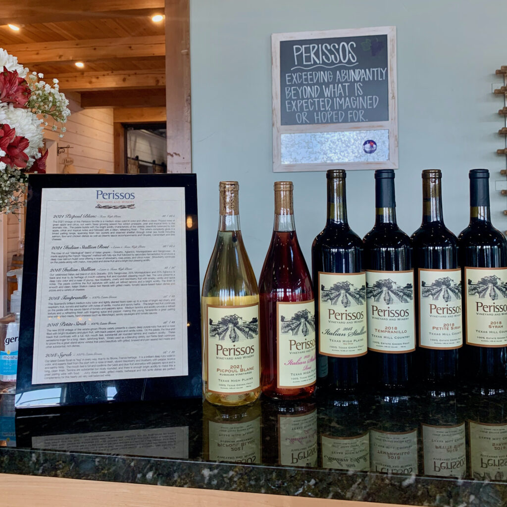 Perissos wines lined up on their bard with a sign behind it that says Perissos: exceeding abundantly beyond what is expected, imagined, or hoped for