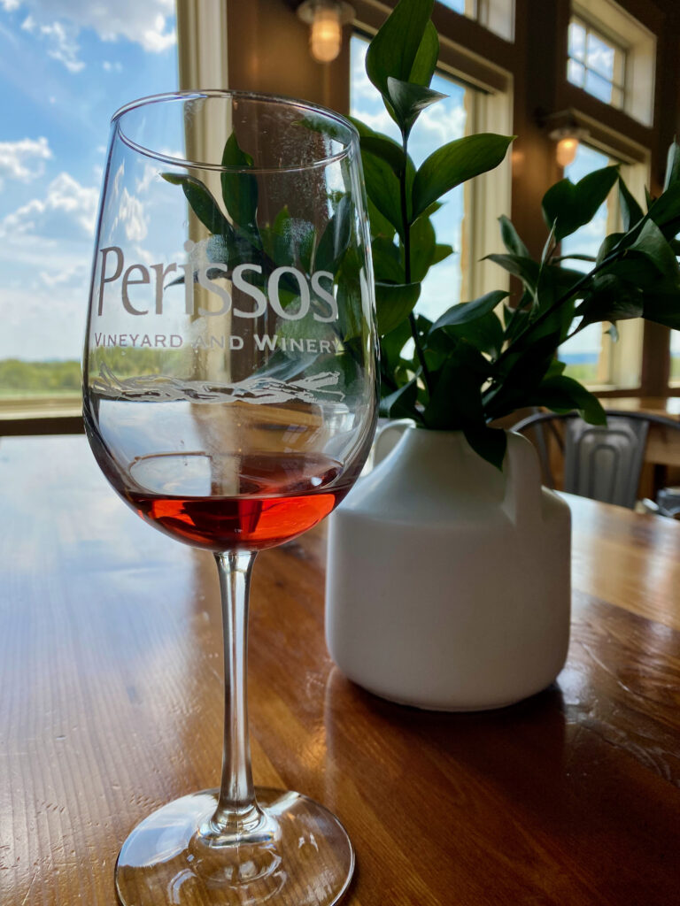 Glass of red wine etched with Perissos logo in front of decorative plant