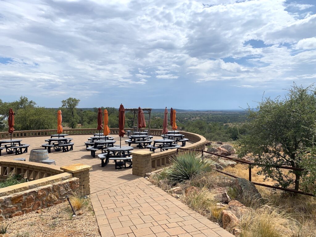 a stone patio with tables and umbrellas in various shades of orange overlooking a valley in the Texas hill country